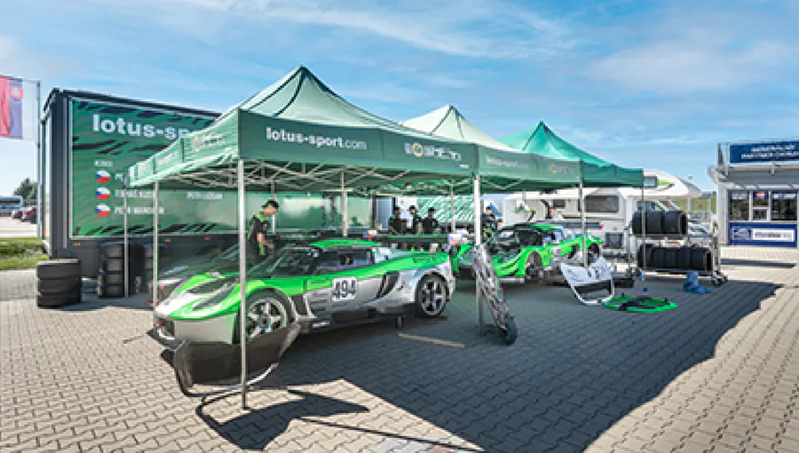 Tým KT MOTORSPORT v boxech se dvěma závodními vozy pod stany lotus-sport.com.