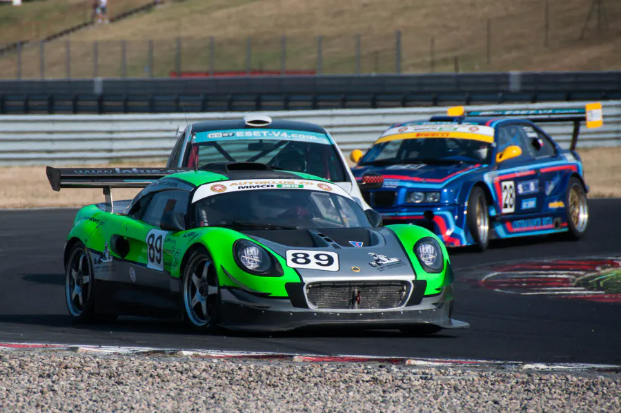 Zelený Lotus Exige číslo 89 vedle modrého vozu jiné třídy před vjezdem do zatáčky.